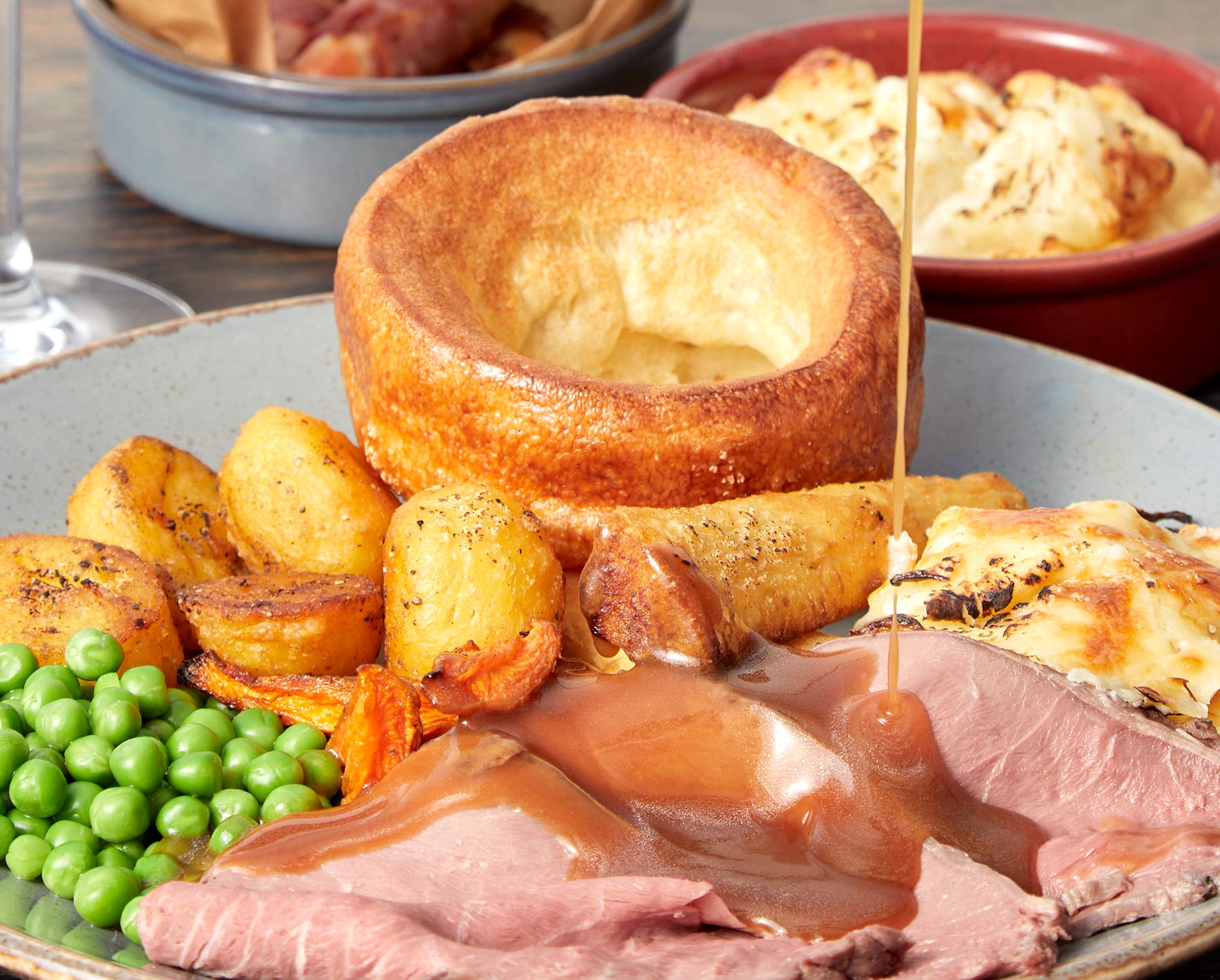 Roast beef, roast potatoes, Yorkshire Pudding, carrots with cauliflower cheese in background